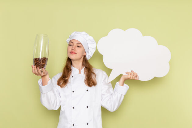 脸身着白色厨师服的女厨师手持绿色墙上的白色标牌的正面视图举行漂亮厨房
