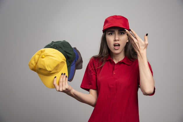 快递愤怒的送货员穿着红色制服 手里拿着五颜六色的帽子女职业制服