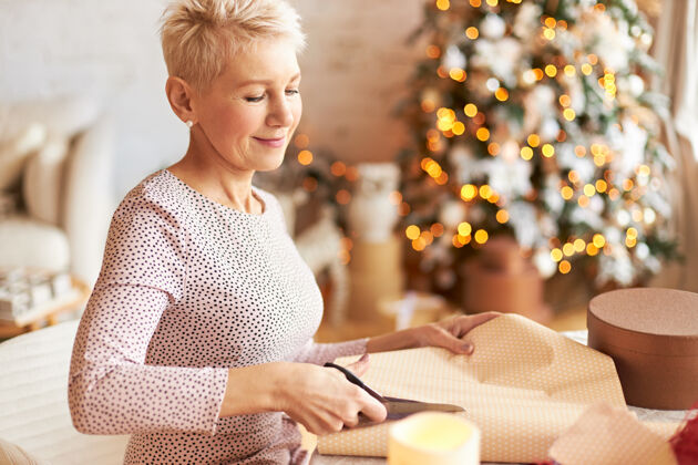 惊喜节日 庆祝和假期的概念优雅美丽的成熟女子短发摆在装饰客厅圣诞树 剪礼物包装剪刀包装自制圣诞节
