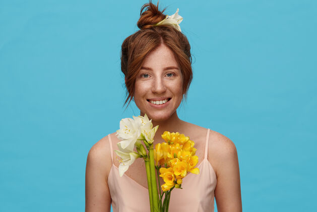 结年轻开朗的红发女士的肖像 自然的妆容 带着迷人的微笑看着镜头 手里拿着一束鲜花 隔离在蓝色的背景下红发微笑花