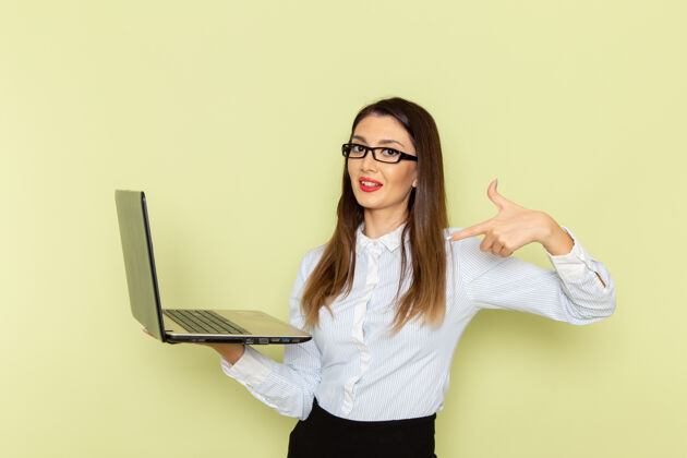 工作身穿白衬衫和黑裙子的女上班族在绿色墙上手持和使用笔记本电脑的正面图衬衫忙碌抱着