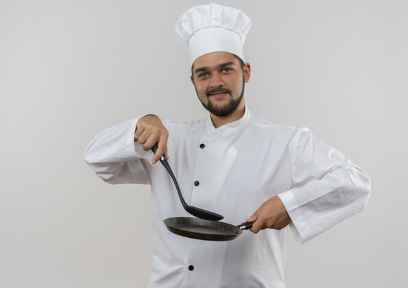 制服年轻的男厨师穿着厨师制服 手里拿着开槽汤匙和煎锅 被隔离在空白处请拿着薯条