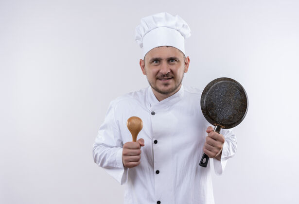 锅面带微笑的年轻帅哥厨师身着厨师制服 手里拿着勺子和煎锅隔离在空白处薯条勺子制服
