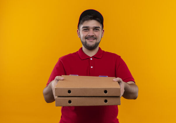 年轻人年轻的送货员身穿红色制服 头戴鸭舌帽 手里拿着一叠披萨盒 看上去自信满面笑容红色叠着拿着
