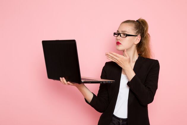 人员身穿黑色夹克的女上班族正拿着笔记本电脑站在浅粉色的墙上女性前面女职员