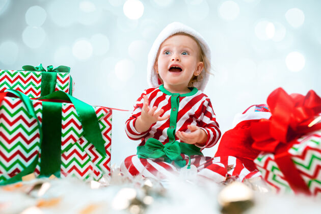 红色可爱的女婴1岁 戴着圣诞帽 拿着礼物在圣诞装饰上摆姿势拿着圣诞球坐在地板上圣诞节帽子漂亮