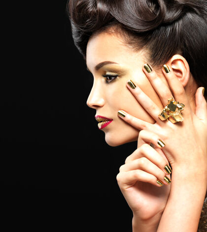 戒指美丽的黑发女人 金色的指甲和时尚的眼妆-在黑色的墙上外形魅力女人