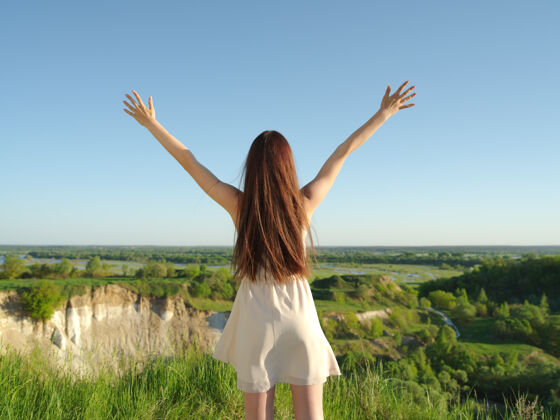 手在大自然中 一个轻松快乐的年轻女子举起双臂站在户外安静的女孩站在悬崖边享受夏天-户外草地和平快乐