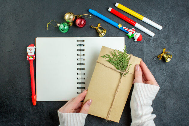 视图手的顶视图螺旋笔记本上的礼物与新年快乐写作装饰配件黑色背景学校信封圣诞节