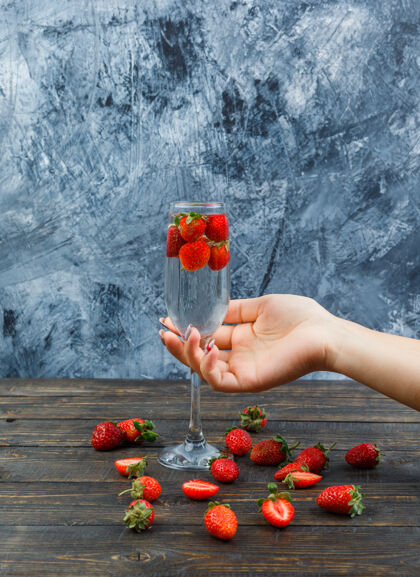 路径手持酒杯和草莓在酒杯上的深色石头表面侧视图多汁酒美味