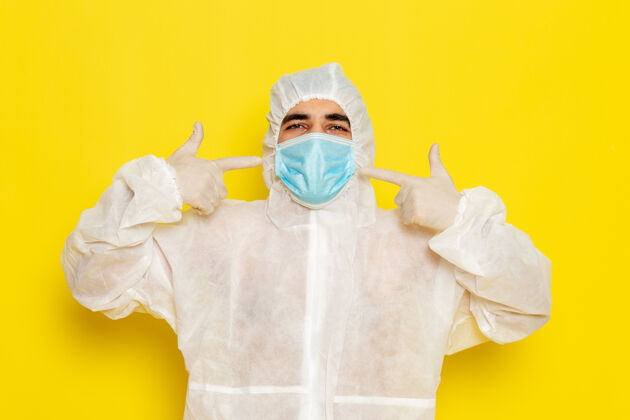 正面黄色墙壁上戴着面具的穿着白色特殊防护服的男科学工作者的正面图危险工人套装