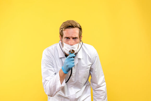 男性正面图戴着口罩的男医生 黄色背景上戴着听诊器 健康人冠状病毒仪器