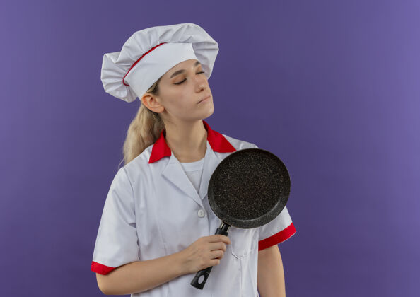 和平安静的年轻漂亮的厨师 穿着厨师制服 拿着煎锅 闭着眼睛 孤立在紫色的空间里厨师漂亮紫色