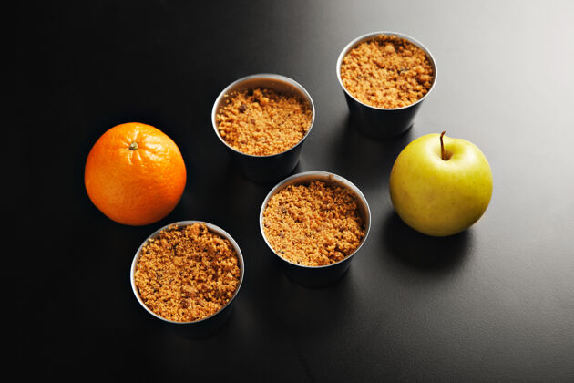 碎的介绍四个相同的不锈钢杯与苹果碎甜点 一个橙色和一个黄色的苹果拍摄从顶部在黑色的表皮甜的熟的