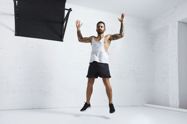 手臂纹身和肌肉运动员做跳跃杰克隔离在白色砖墙旁边的黑色拉杆 看左边手臂美学运动装