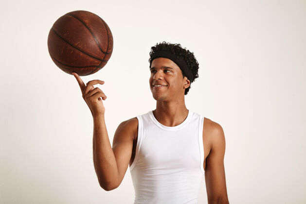 Outdoor一个年轻的非洲裔美国篮球运动员 穿着白色无袖衬衫 一只手指上拿着一个旧皮球ExerciseFingerYoung