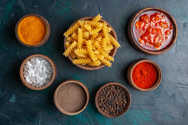面食在深蓝色的桌子上 可以俯瞰形状各异的意大利面食和不同的调味品土豆调味品烹饪