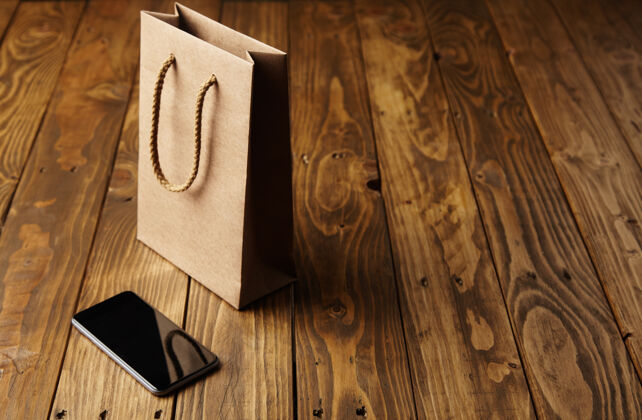 反射浅棕色工艺纸袋反射在一个一尘不染的黑色智能手机躺在旁边的手工木桌上包装技术顶部