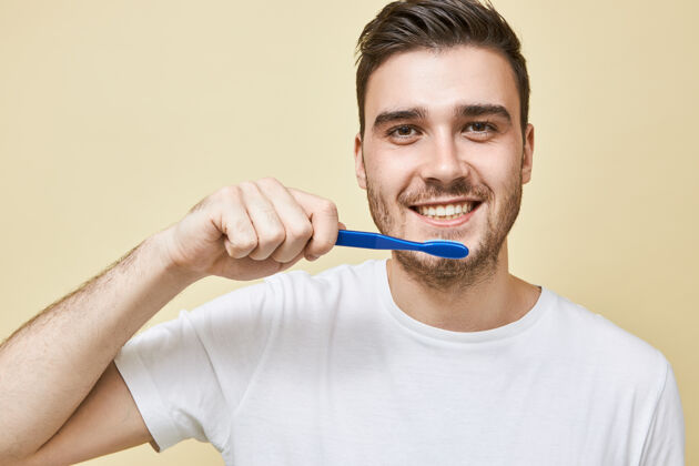 微笑正面未刮胡子的年轻男性手持塑料牙刷 在镜子前的浴室里刷牙 注意牙齿卫生 表情愉快快乐牙齿帅哥