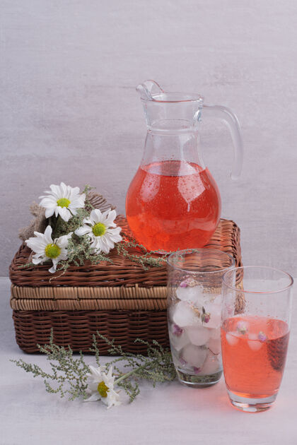 冰白桌子上放着新鲜的柠檬水和带雏菊的罐子罐子篮子柠檬水
