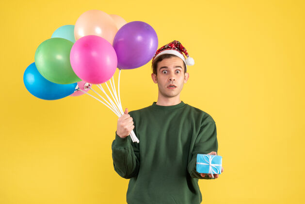 气球正面图大眼睛的年轻人戴着圣诞帽和五颜六色的气球拿着黄色的蓝色礼盒盒子帽子工艺
