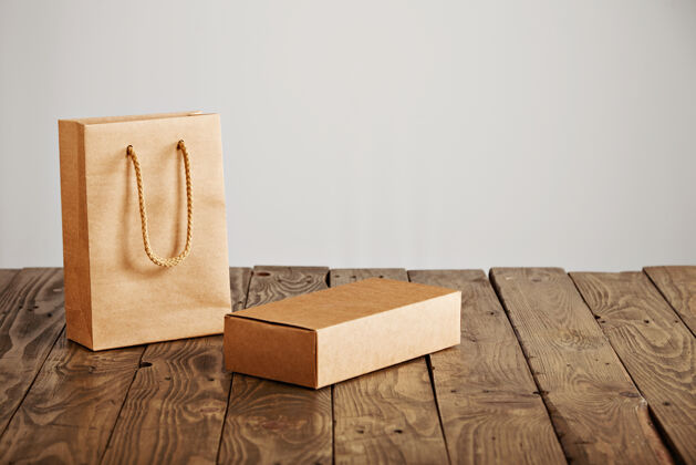 储存未贴标签的工艺纸袋旁边的纸板空白盒提出了乡村木桌上 孤立的白色背景袋子物品邮政