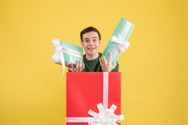 漂亮正面图拿着礼物的年轻人站在黄色的大礼盒后面站着礼品盒年轻人