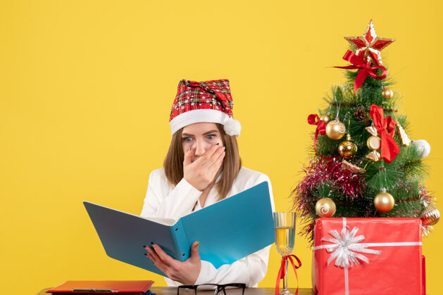 坐着前视图女医生坐在圣诞礼物持有黄色背景文件圣诞节电脑办公室