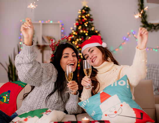 扶手椅快乐的年轻女孩们拿着香槟和火花杯坐在扶手椅上 在家里享受圣诞节时光圣诞节香槟坐着