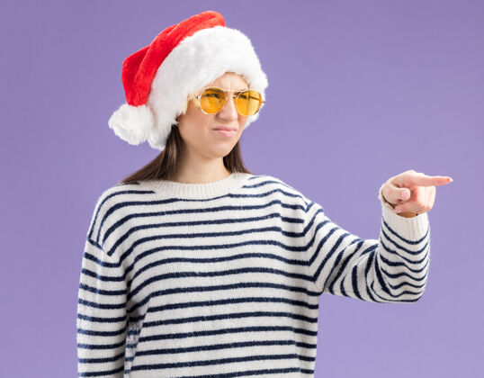 帽子戴着太阳眼镜 戴着圣诞帽的年轻白种人姑娘 面目全非 指指点点指向圣诞年轻