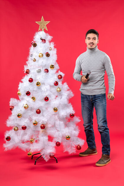 圣诞站在红色装饰的圣诞树旁 积极的家伙在唱歌 新年气氛的垂直视图心情圣诞树歌曲