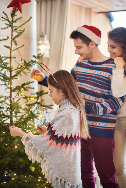 服装父母带着孩子挂圣诞装饰品圣诞树十二月悬挂