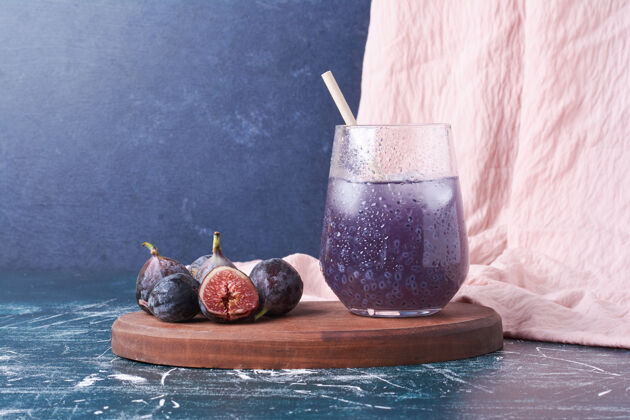 美味紫色无花果配一杯果汁在蓝色上健康热带玻璃