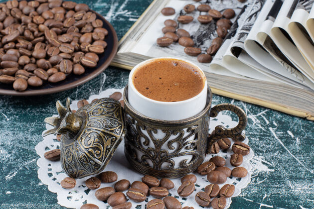 美味一杯泡沫咖啡 一盘咖啡豆和一本大理石桌上的书书籍饮料热的