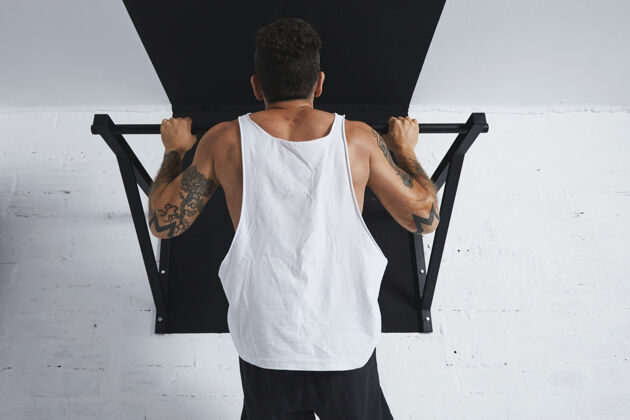 身体肌肉发达的男运动员在白色空白坦克t恤显示健美操动作拉上拉杆 保持在顶部运动运动场运动装