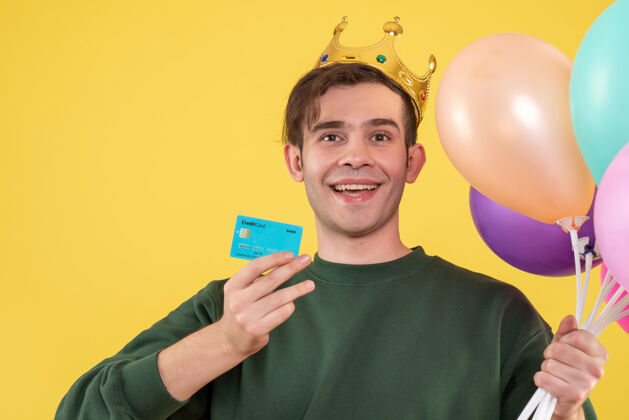 持有正面图帅哥戴着皇冠手持气球和黄色卡片气球年轻男人