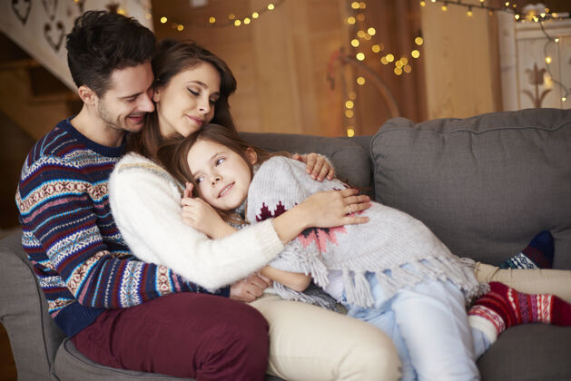 假期快乐的父母和在沙发上放松的女孩父母十二月看着