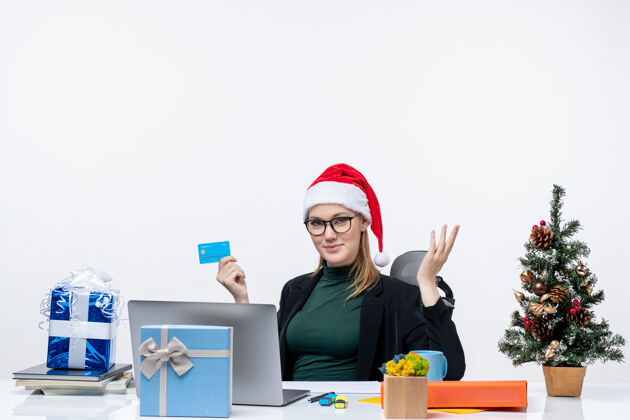 商人戴着圣诞老人帽 戴着眼镜的漂亮女人坐在桌子旁 手里拿着银行卡在办公室问些什么漂亮的桌子电脑