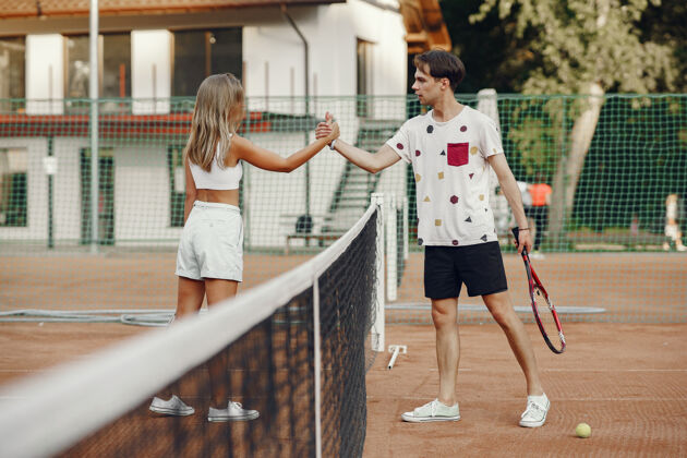 团队网球场上的一对年轻夫妇两个穿着运动服的网球运动员娱乐球拍球