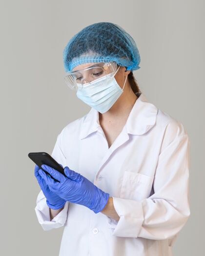 安全戴着安全眼镜和医用面罩手持智能手机的女科学家的前视图实验手套炼金术