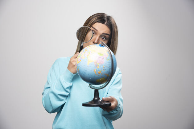 工人穿着蓝色运动衫的金发女孩拿着一个地球仪 用放大镜寻找目的地人世界雇员