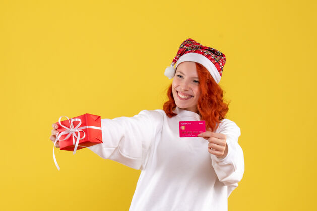银行圣诞礼物和黄墙上银行卡的年轻女子的正面图圣诞节年轻美丽