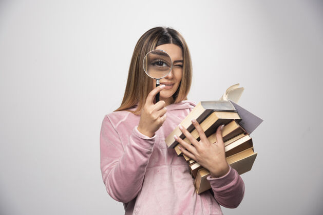 聪明一个穿着粉色衬衫的女孩手里拿着一堆书 正试着用放大镜看上面的书呢信件成人年轻