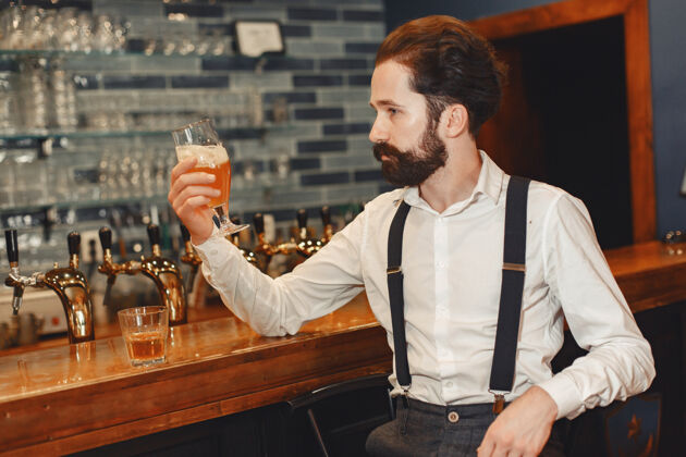 威士忌一个留着胡子的男人站在吧台旁 喝着酒杯里的酒白兰地啤酒啤酒厂