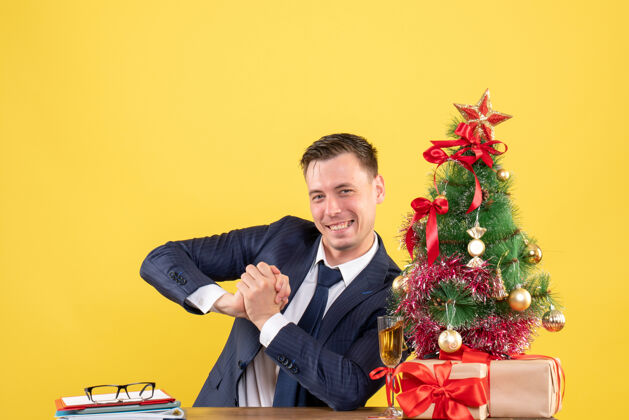 黄色笑容可掬的帅哥坐在圣诞树旁的桌子前 黄色的礼物礼物男性男人