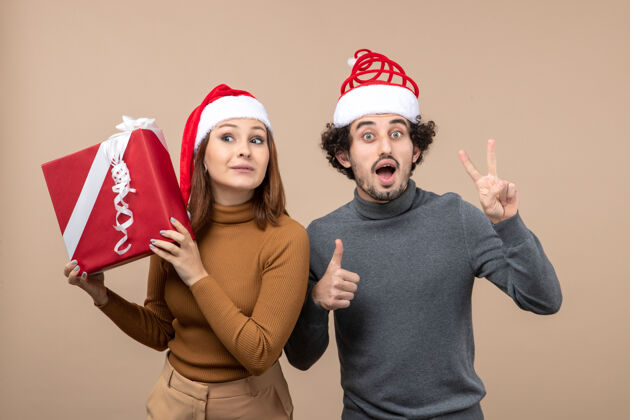 情侣新年气氛喜庆的概念与有趣兴奋的年轻可爱的夫妇戴着红色圣诞老人帽灰色圣诞节庆祝帽子