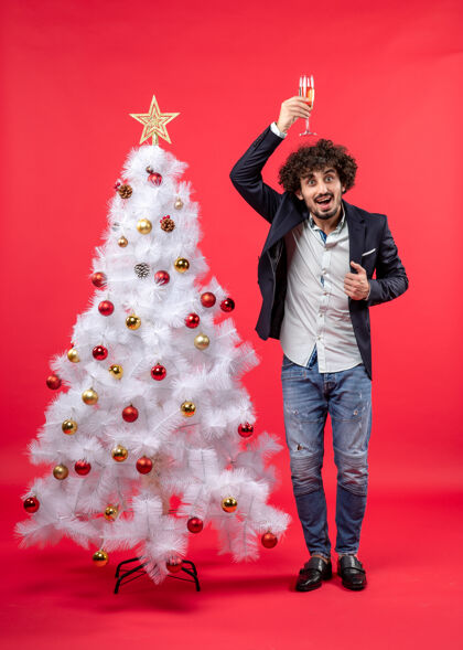 酒年轻人头上顶着一杯葡萄酒 在装饰过的白色圣诞树旁庆祝新年圣诞年轻人圣诞树
