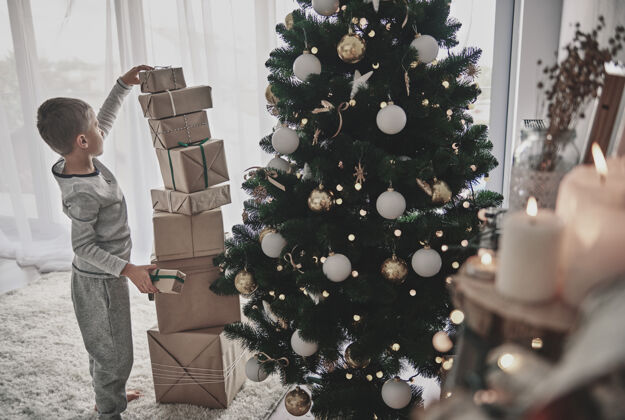 盒子男孩把圣诞礼物堆在圣诞树旁边圣诞节删除侧视图
