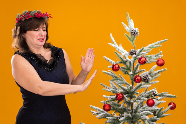 头一个戴着圣诞花环 脖子上戴着金属丝花环的中年妇女站在装饰好的圣诞树旁女人拒绝圣诞节