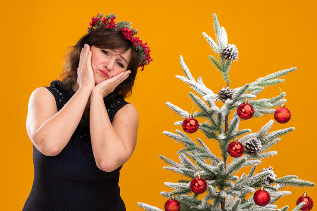 圣诞悲伤的中年妇女戴着圣诞花环 脖子上戴着金属丝花环 站在装饰好的圣诞树旁站着金箔相机